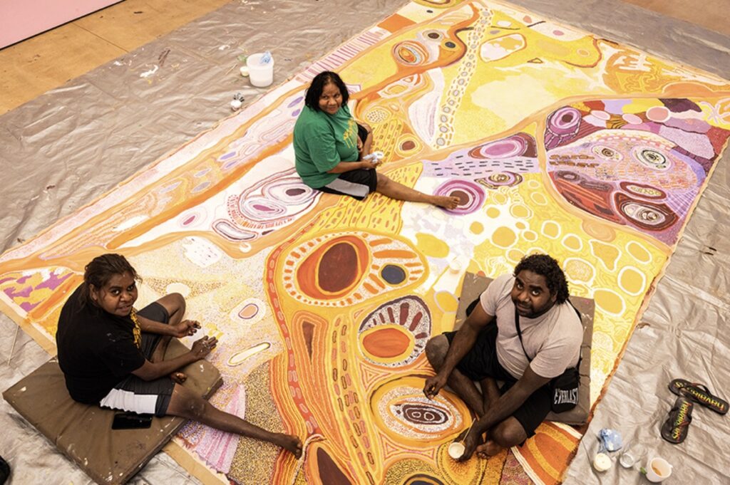 Martumili Artists painting on a large colourful canvas